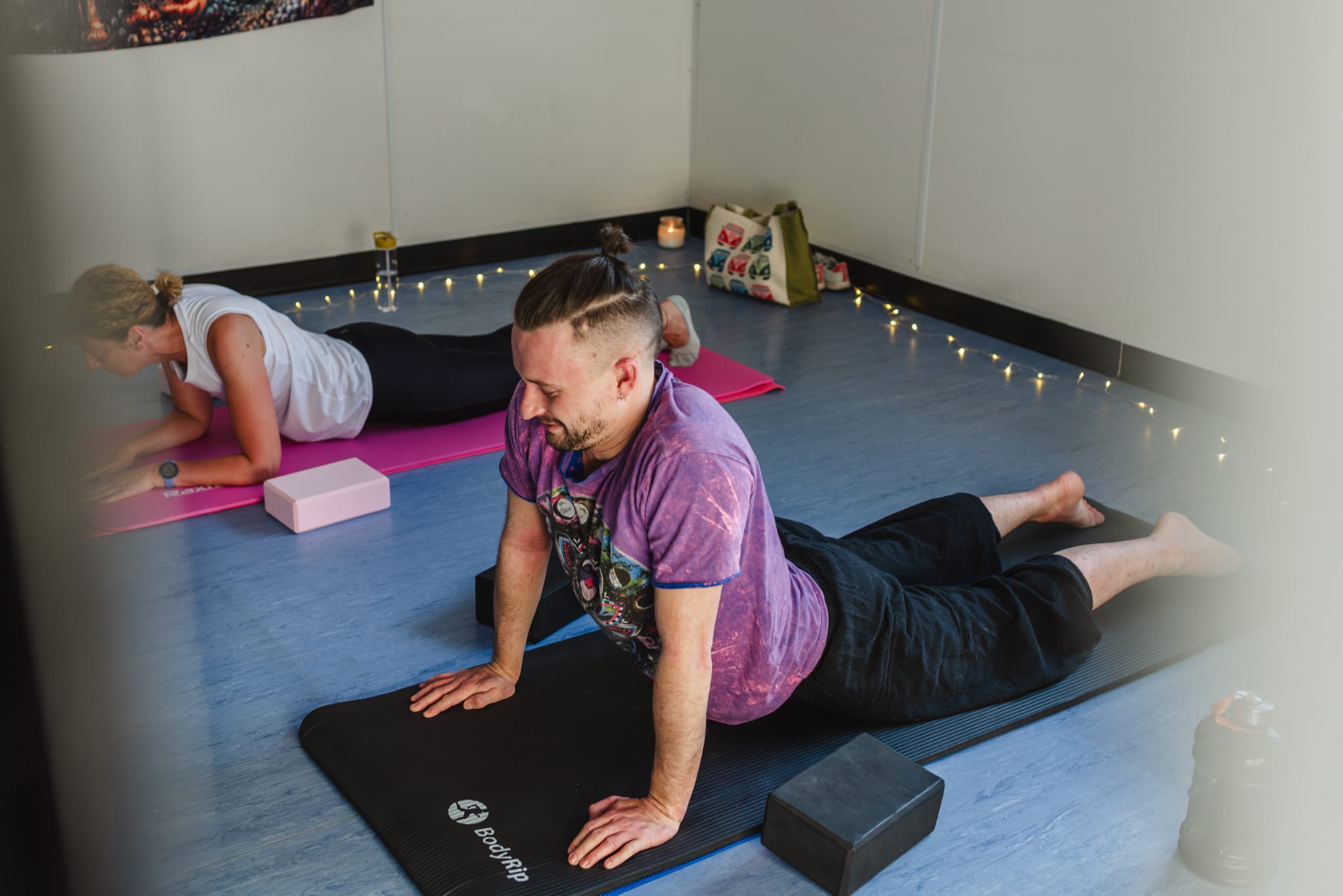 A man and woman practising floor-based yoga poses on mats in a candlelit studio